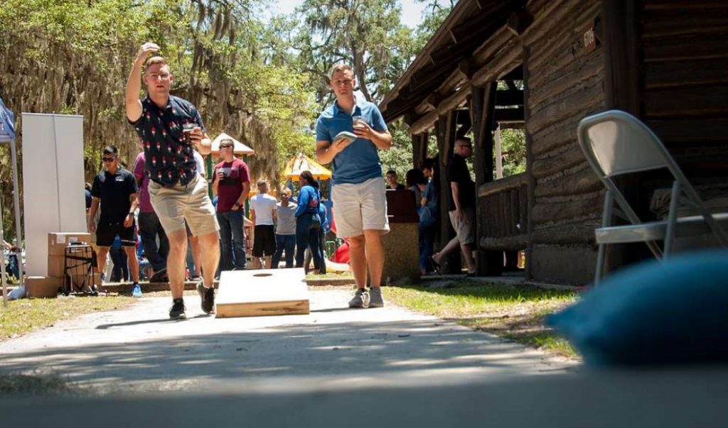 guys playing cornhole with drinks